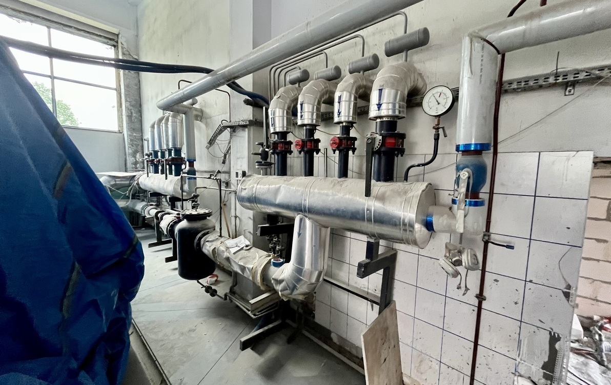 Zdjęcie przedstawia instalację złożoną z rur i złaczek, zamontowaną na ścianie
