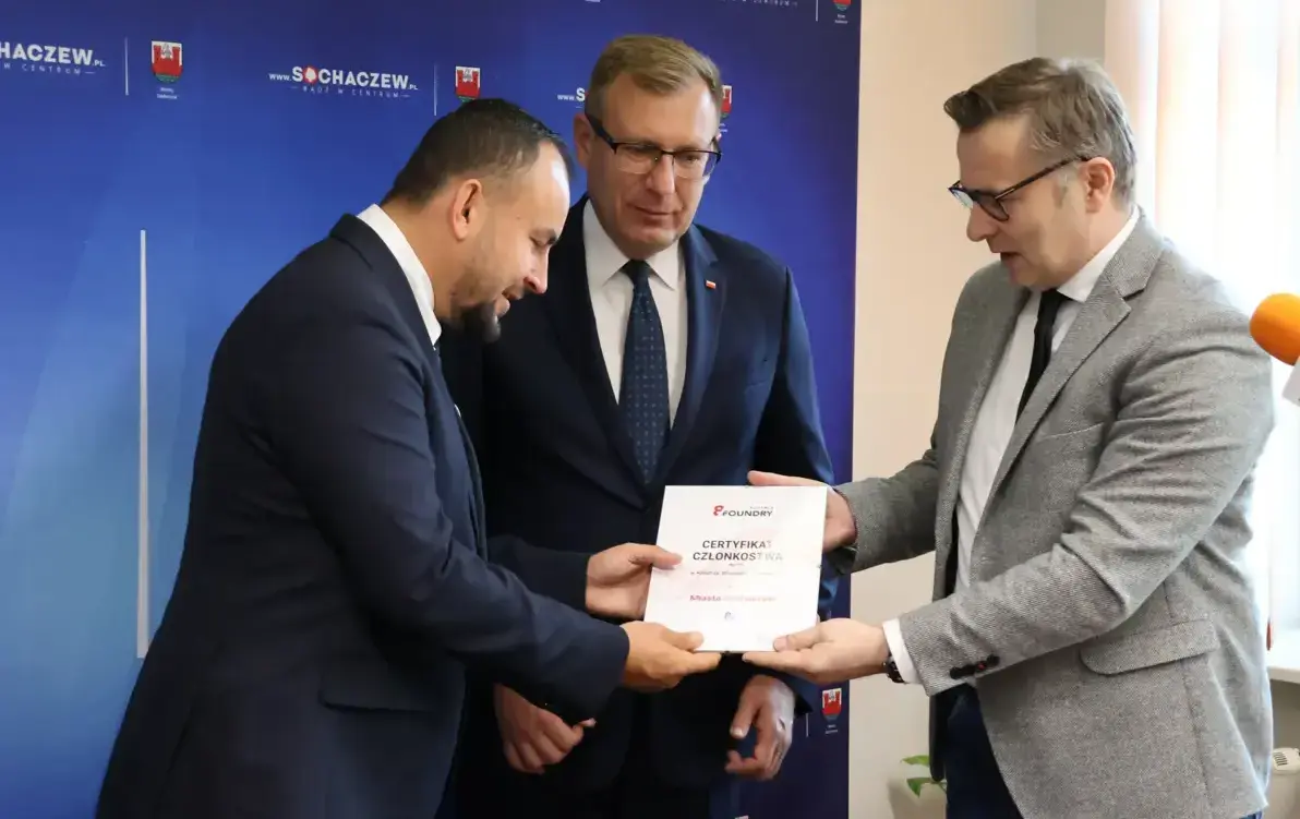 Zdjęcie przedstawia trzech mężczyzn przekazujących sobie dokument