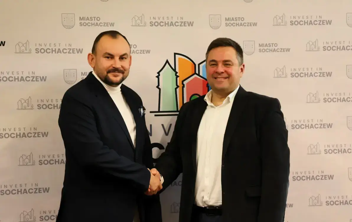 Zdjęcie przedstawia dwóch mężczyzn podających sobie ręce na tle ścianki z napisem Invest in Sochaczew