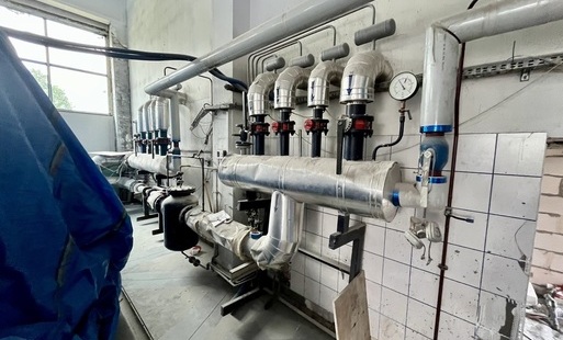 Zdjęcie przedstawia instalację złożoną z rur i złaczek, zamontowaną na ścianie