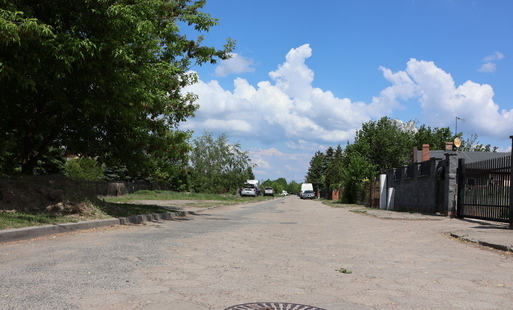 Zdjęcie przedstawia widok na nawierzchnię ulicy z trylinki, w głębi drzewa i samochody