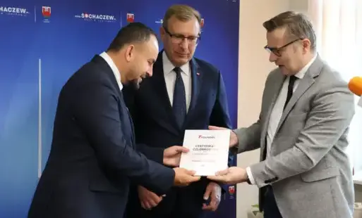 Zdjęcie przedstawia trzech mężczyzn przekazujących sobie dokument